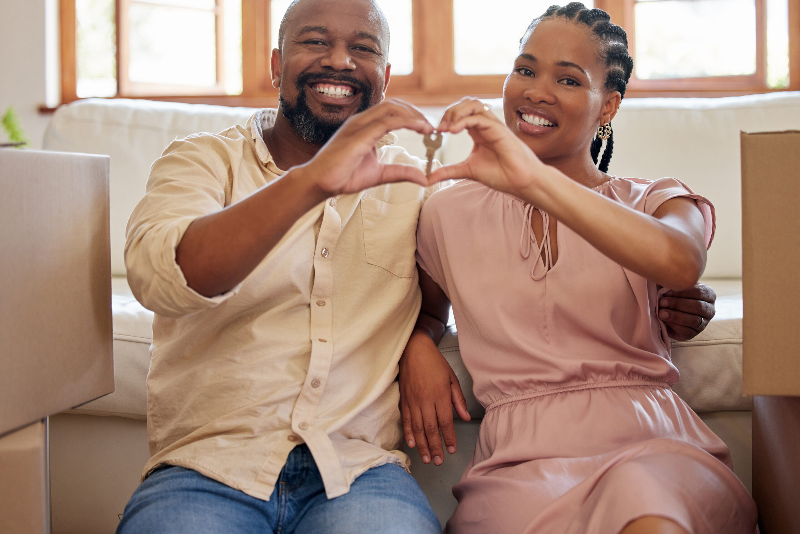 A couple holding keys, making a heart sign with their hands at home. Portrait of a smiling, happy a.