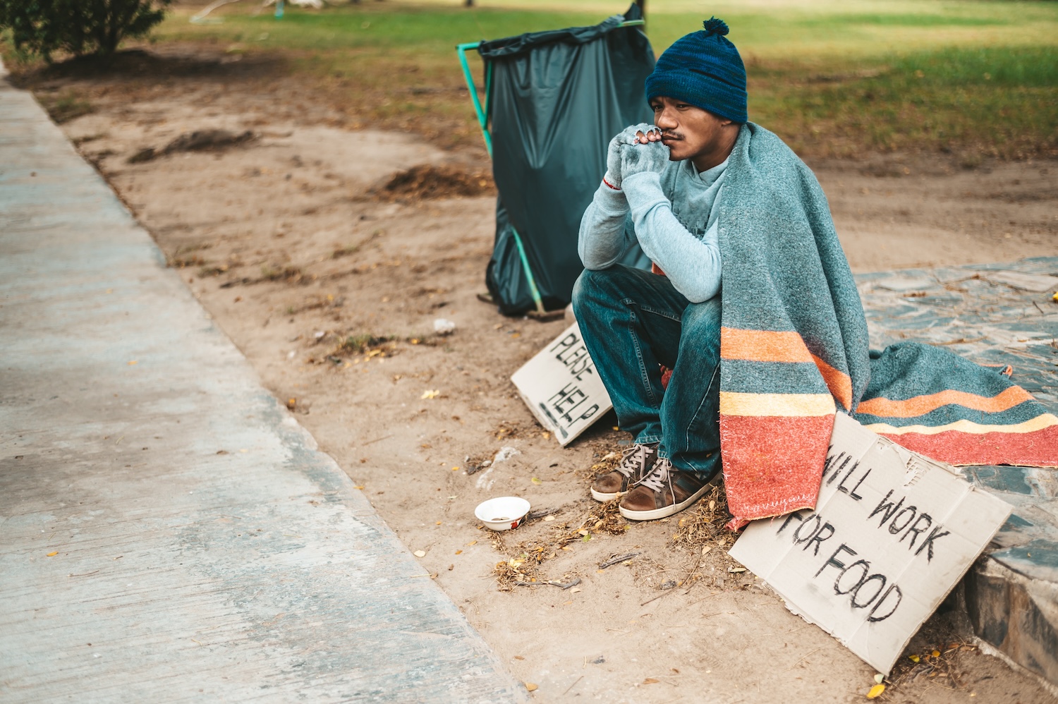 a man sitting beggars with homeless please help message. Selective focus.