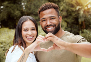 Couple, happy and hand heart sign in a nature park showing love and a smile outdoor. Black people w.