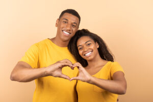 Loving african american couple cuddling and making together heart shape gesture with their hands as a sign of their love, peach studio background. Valentine concept