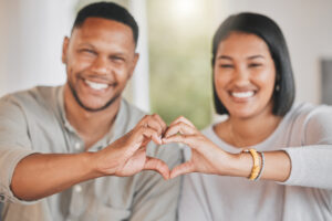 Portrait of a young couple making a heart shape with their hands at home.