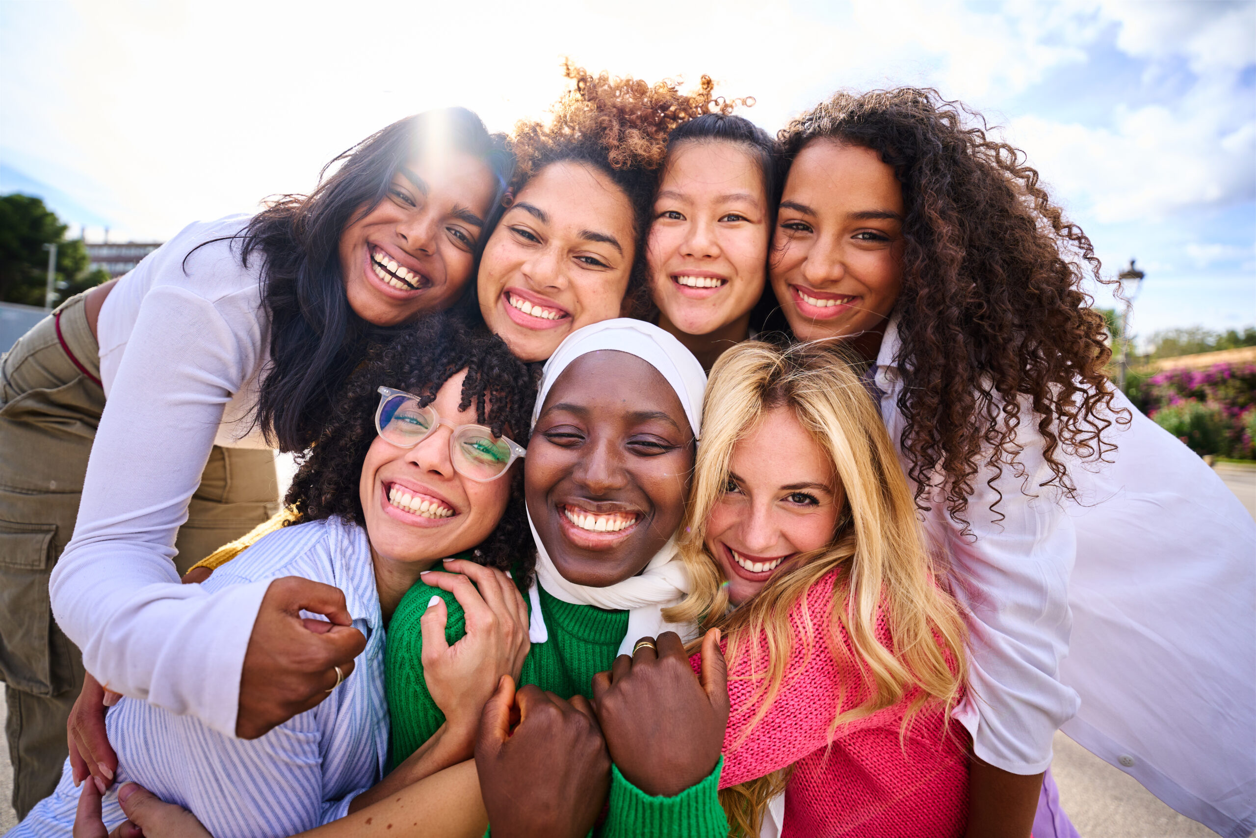 Portrait of group of beautiful young multiracial girl friends community hugging and looking at camera outdoor. Smiling only women together embraced affectionately. Female friendships and quality time