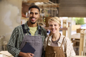 Portrait Of Male And Female Apprentices Working As Carpenters In Furniture Workshop