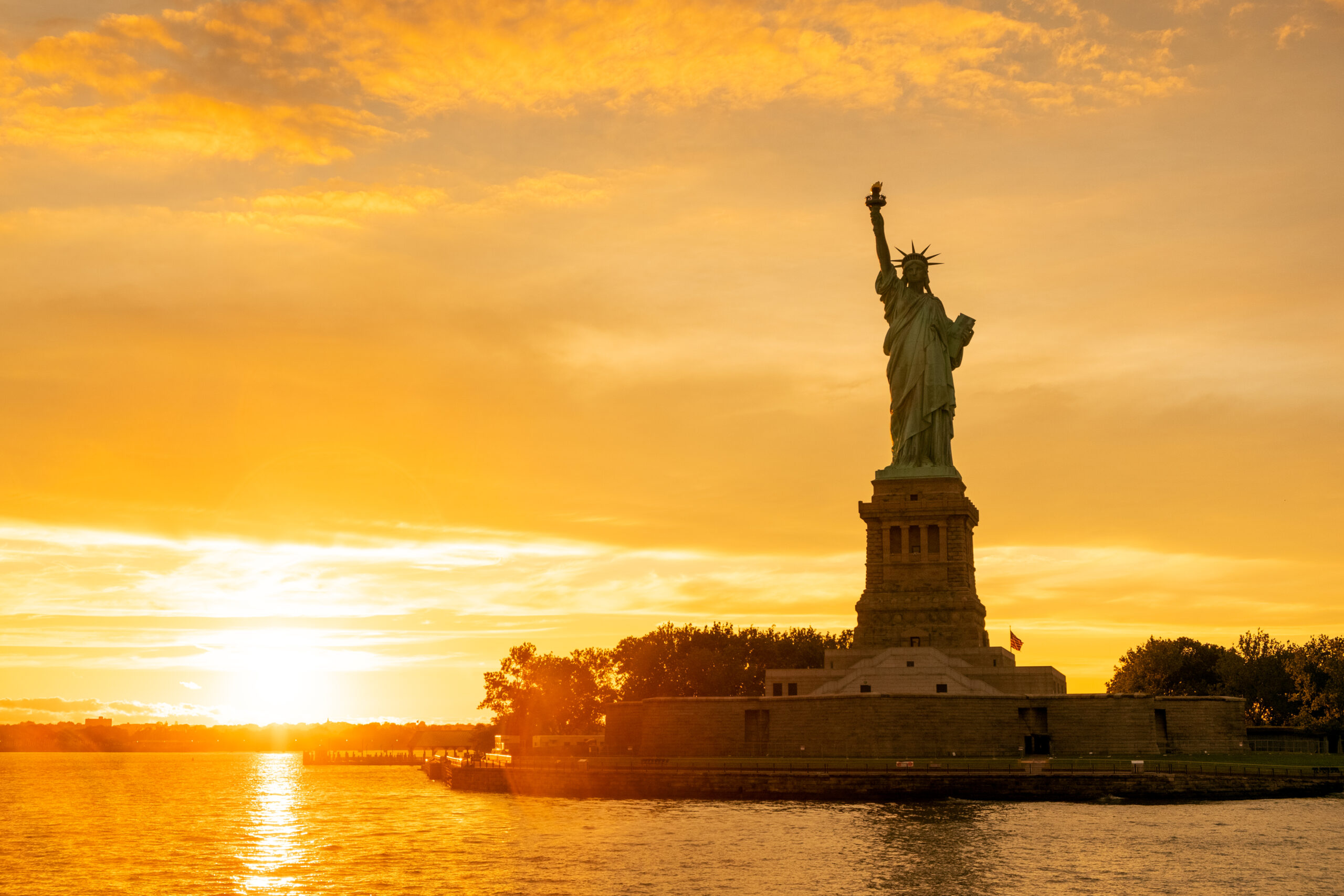 The Statue of Liberty at New York city during sunset with reflections on the ocean