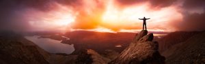 Magical Fantasy Adventure Composite of Man Hiking on top of a rocky mountain peak. Background Landscape from Yukon, Canada. Sunset or Sunrise Colorful Sky