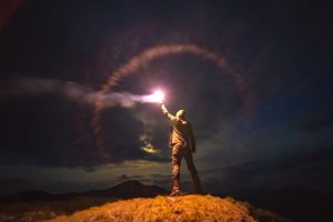 The male with a bright firework stick standing on a mountain. evening night time